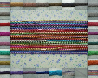 Può includere: Assortimento di catene di perline colorate, tra cui oro, argento, rosso, blu, verde, viola e bianco. Le catene sono disposte in file su uno sfondo bianco con un motivo floreale.