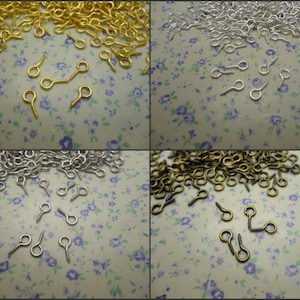 May include: Assortment of small, gold, silver, and bronze eyelet screw findings. The findings are scattered on a white background with a floral pattern.