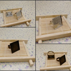 Op de afbeelding: Vier vierkante ringblanken op houten standaards. Twee zijn zilver en twee zijn brons.