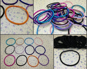 May include: Assortment of colorful hair elastics in various sizes and colors, including pink, purple, blue, black, and orange. The hair ties are arranged in a pile and on a white surface with a floral pattern.