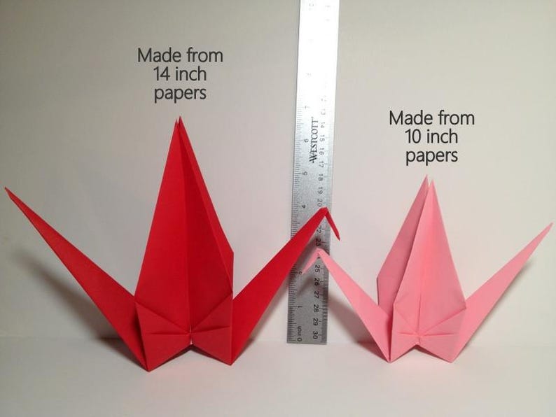 May include: Two origami cranes, one red and one pink, are displayed next to a ruler. The red crane is made from 14-inch paper, and the pink crane is made from 10-inch paper. The text on the image indicates the paper size used.