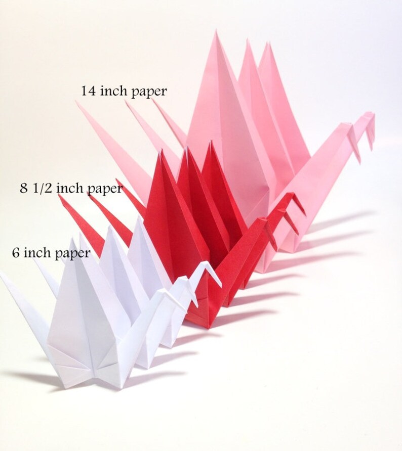 May include: Origami paper cranes in a gradient of colors, from white to pink and red. The cranes are made from 6-inch, 8.5-inch, and 14-inch paper. The cranes are arranged in a row, showcasing the size difference.