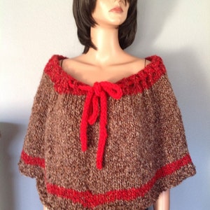Puede incluir: Un poncho de punto marrón y rojo con una corbata de lazo roja. El poncho tiene un punto texturizado y un ribete rojo alrededor del cuello y el dobladillo.