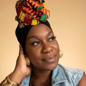 Puede incluir: Un pañuelo para la cabeza con un vibrante patrón geométrico en rojo, amarillo, negro y verde, sobre una base negra sólida. El conjunto incluye pendientes de aro texturizados en tono dorado y una pulsera de brazalete de metal dorado pulido.