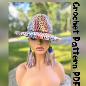 May include: A crocheted hat with a wide brim and a multi-colored pattern. The hat is made with a variety of shades of blue, pink, and brown yarn. The hat is sitting on a mannequin's head. The text "Crochet Pattern PDF" is written vertically on the right side of the image.