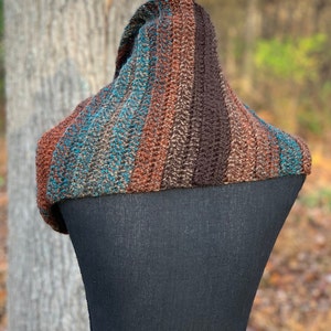 May include: A brown, teal, and orange striped crocheted cowl neck scarf. The scarf is draped over a black dress form.