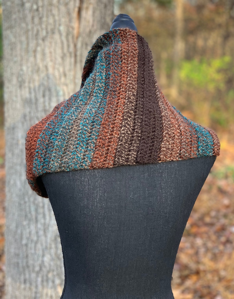 May include: A brown, teal, and orange striped crocheted cowl neck scarf. The scarf is draped over a black dress form.