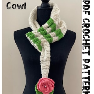Puede incluir: Un cuello de crochet a rayas blancas y verdes con una flor de crochet rosa y verde adjunta. El cuello se muestra en un maniquí negro. El texto "Cowl" está en la esquina superior izquierda de la imagen. El texto "PDF CROCHET PATTERN" está en la esquina superior derecha de la imagen.