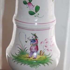 May include: White ceramic sugar shaker with a red rim and hand-painted floral and figural designs. The shaker has a domed lid with holes for sprinkling sugar.