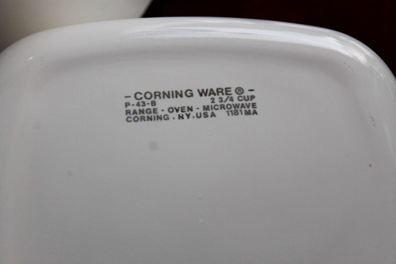 Może przedstawiać: Zbliżenie białego naczynia Corning Ware z zaokrąglonymi rogami. Tekst na naczyniu brzmi "- CORNING WARE - P-43-B 2 3/4 CUP RANGE - OVEN - MICROWAVE CORNING. NY. USA 1181 MA."