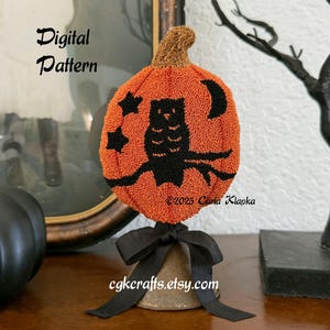 May include: Orange pumpkin-shaped decoration with a black owl design, stars, and a crescent moon. The pumpkin has a brown stem and sits atop a bell with a black bow. Text on the image reads "Digital Pattern" and "cgkcrafts.etsy.com".