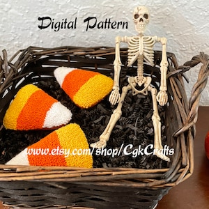 Puede incluir: Tres juguetes de peluche con forma de maíz dulce naranja, blanco y amarillo en una cesta de mimbre marrón con papel triturado negro. Un esqueleto de plástico se sienta en la cesta. El texto "Digital Pattern" está por encima de la cesta. El texto "www.etsy.com/shop/CgkCrafts" está debajo de la cesta.