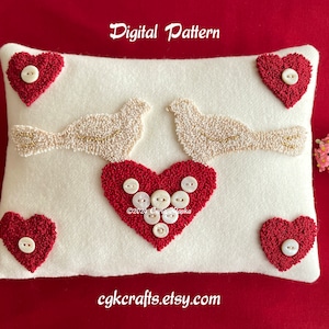 Puede incluir: Almohada blanca con un corazón rojo y dos pájaros blancos bordados con cuentas blancas. La almohada tiene un corazón rojo con botones blancos en el centro. La almohada está sobre un fondo rojo.  "Digital Pattern" y "cgkcrafts.etsy.com" están impresos en la almohada.
