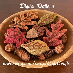 May include: A digital pattern for needle felting autumn leaves. The pattern includes a variety of leaves in different colors, including red, orange, yellow, and green. The leaves are arranged in a bowl with pine cones.