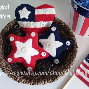 May include: Three handmade plush patriotic stars and a heart-shaped American flag pillow in a wicker basket. The stars are red, white, and blue, and the heart is red, white, and blue with white buttons. The basket is brown and wicker.