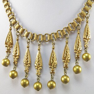 May include: A gold necklace with a chain and multiple teardrop-shaped pendants. Each pendant has a floral design and is attached to a round bead.
