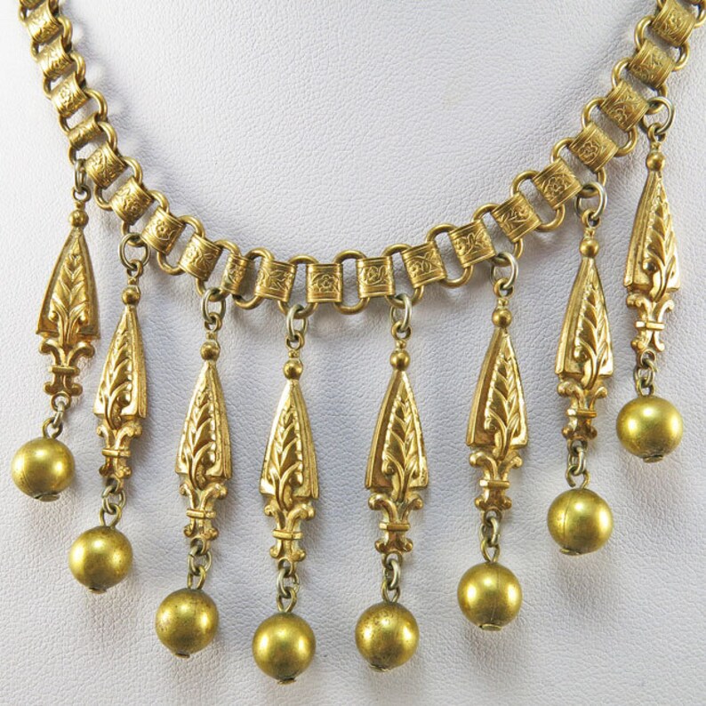 May include: A gold necklace with a chain and multiple teardrop-shaped pendants. Each pendant has a floral design and is attached to a round bead.