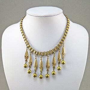 May include: A gold-tone necklace with a chain and multiple dangling teardrop-shaped charms. Each charm has a detailed floral design and is accented with a round gold bead.