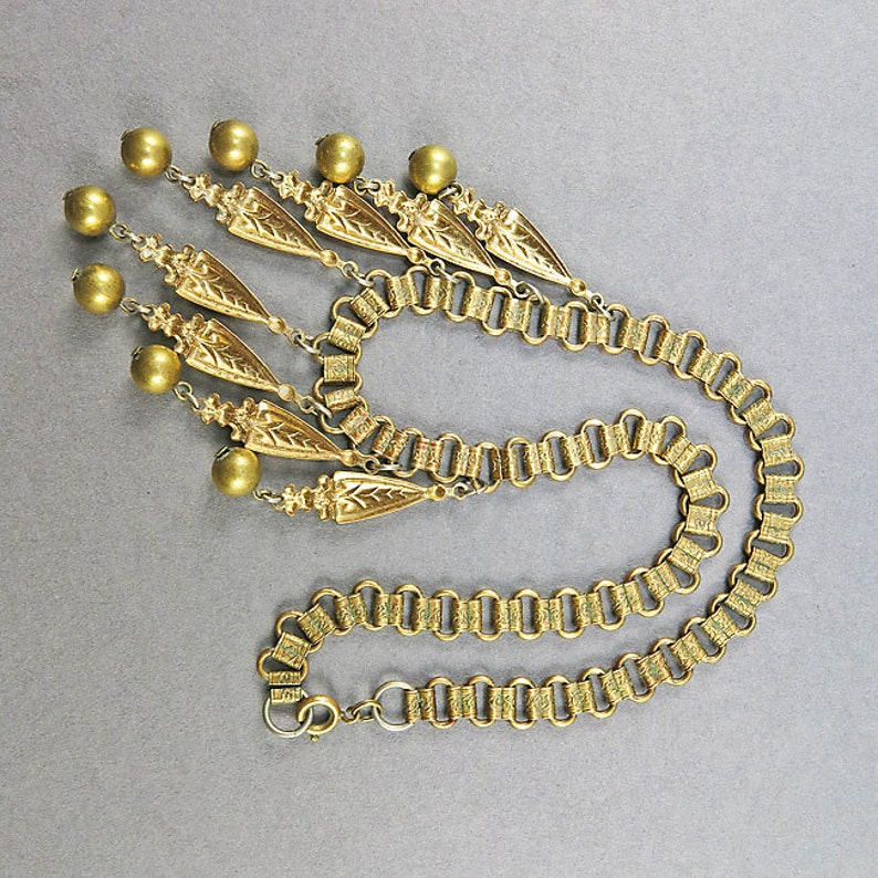 May include: A gold necklace with a chain and a pendant made of multiple gold beads and leaf-shaped charms.