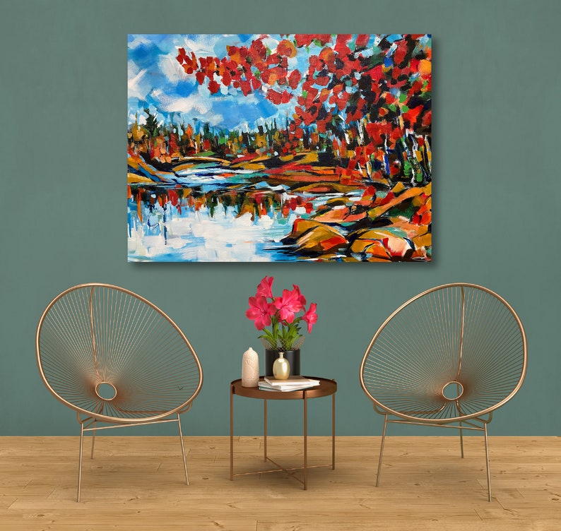 May include: A painting of a colorful landscape with a lake and trees in the foreground. The trees are in shades of red, orange, and yellow, and the lake is a deep blue. The painting is framed and hanging on a wall.