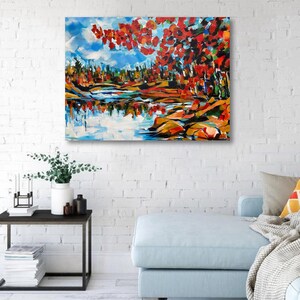 May include: A painting of a lake scene with red, orange, and yellow fall foliage reflected in the water. The trees are on the left side of the painting, and the lake is on the right side. The sky is blue with white clouds.