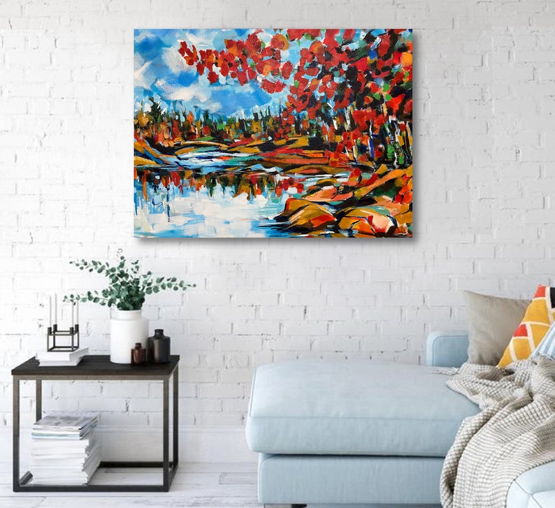 May include: A painting of a lake scene with red, orange, and yellow fall foliage reflected in the water. The trees are on the left side of the painting, and the lake is on the right side. The sky is blue with white clouds.