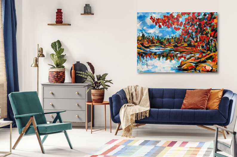 May include: A blue velvet sofa with a throw blanket and two pillows in a living room setting. A painting of a lake scene with red and orange trees hangs on the wall above the sofa.