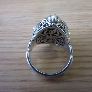 May include: Silver ring with an ornate design. The ring is open and the inside of the band is visible.