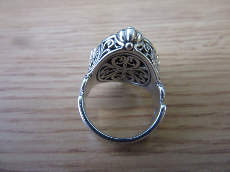 May include: Silver ring with an ornate design. The ring is open and the inside of the band is visible.