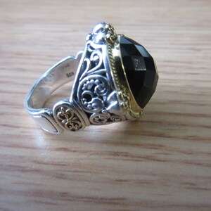 May include: A silver ring featuring a black gemstone and gold accents. The ring has an intricate design with filigree details.