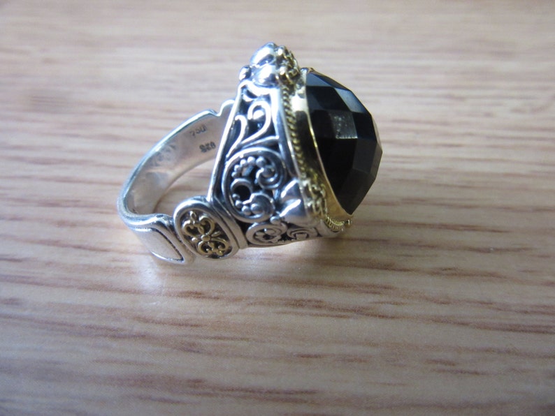 May include: A silver ring featuring a black gemstone and gold accents. The ring has an intricate design with filigree details.