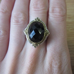 May include: A black gemstone ring with a gold and silver setting. The ring has a large oval-shaped gemstone with a faceted design.