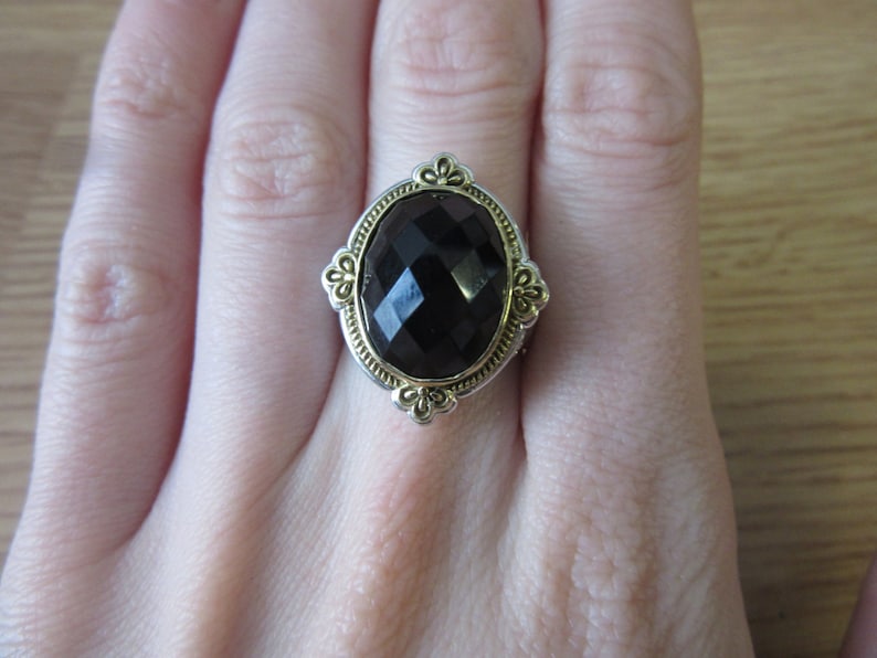 May include: A black gemstone ring with a gold and silver setting. The ring has a large oval-shaped gemstone with a faceted design.