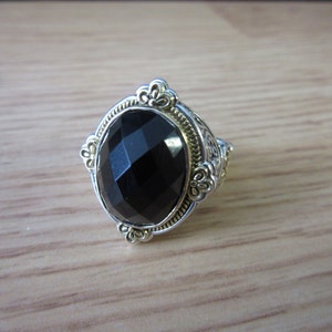 May include: A silver ring featuring a black oval gemstone set in a gold-toned filigree design.