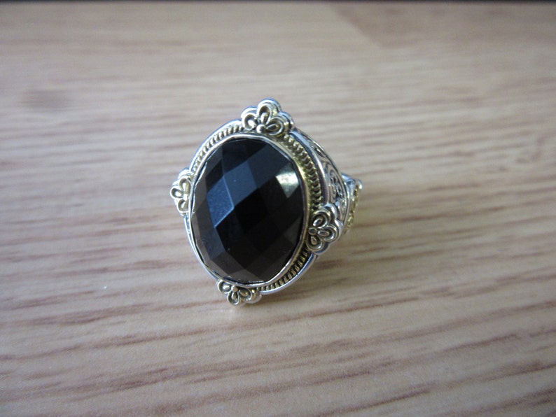 May include: A silver ring featuring a black oval gemstone set in a gold-toned filigree design.