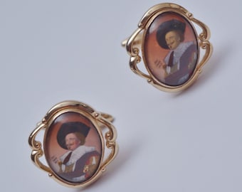Para zabytkowych spinek do mankietów firmy Stratton, The Laughing Cavalier, sygnowanych na cześć Franza Halsa, złocone i malowane na odwrocie szkło, lata 20. XX wieku, angielskie