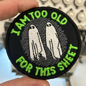 May include: A black and green embroidered patch with two white ghosts and the text "I am too old for this sheet".