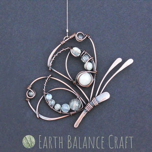 K&ouml;nnte beinhalten: Kupferdraht-Schmetterling mit wei&szlig;en und klaren Glasperlen. Der Schmetterling h&auml;ngt an einer Schlaufe aus Kupferdraht.