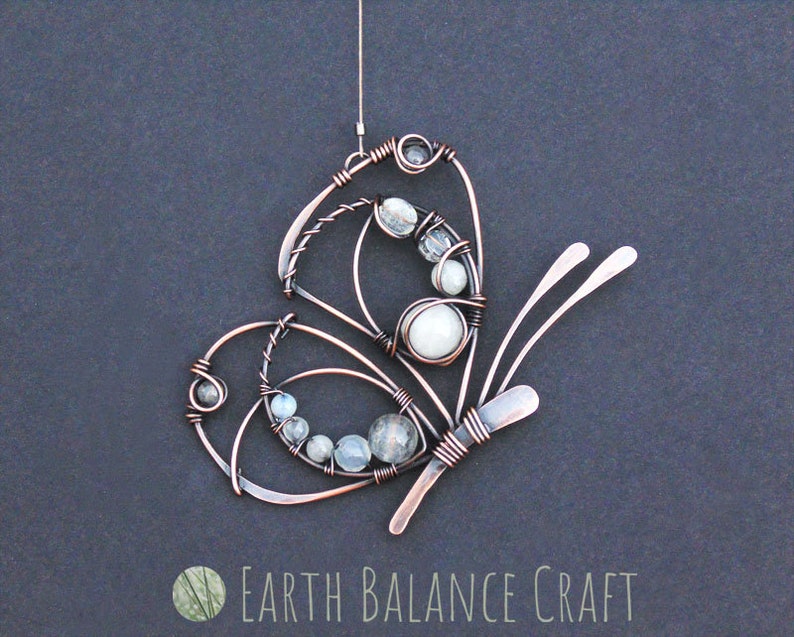 K&ouml;nnte beinhalten: Kupferdraht-Schmetterling mit wei&szlig;en und klaren Glasperlen. Der Schmetterling h&auml;ngt an einer Schlaufe aus Kupferdraht.