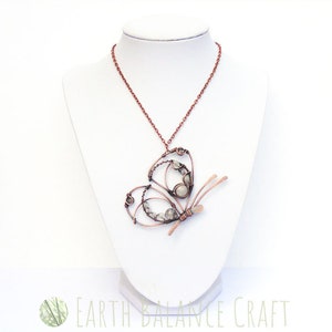 K&ouml;nnte beinhalten: Eine Halskette aus Kupferdraht mit einem Schmetterlingsanh&auml;nger mit wei&szlig;en Steinen. Der Schmetterling ist aus Kupferdraht gefertigt und hat ein filigranes Design.