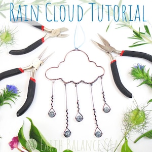 Op de afbeelding: Een DIY-knutselproject voor het maken van een regenwolk-mobiel. De afbeelding toont een wolkvorm van koperdraad met koperdraadstrengen die er vanaf hangen. Elke streng heeft een kleine glazen kraal aan het einde, die regendruppels voorstelt. De afbeelding toont ook twee tangen, die worden gebruikt om de draad te buigen en te vormen.