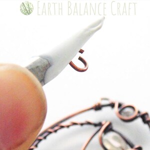 K&ouml;nnte beinhalten: Nahaufnahme eines Kupferdrahts, der mit einem wei&szlig;en Werkzeug zu einer Schleife gebogen wird. Die Schleife wird am Ende des Drahtes gebildet.