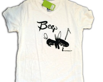 May include: Off-white t-shirt with a black graphic of an insect and the word "Beep" in a handwritten style. The shirt has short sleeves and a crew neck. A green tag is attached near the neckline.
