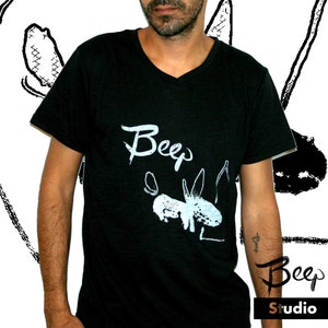May include: Black V-neck t-shirt with the word "Beep" in white script and a white illustration of a creature. The shirt also features the text "Beep Studio" in a stylized font.