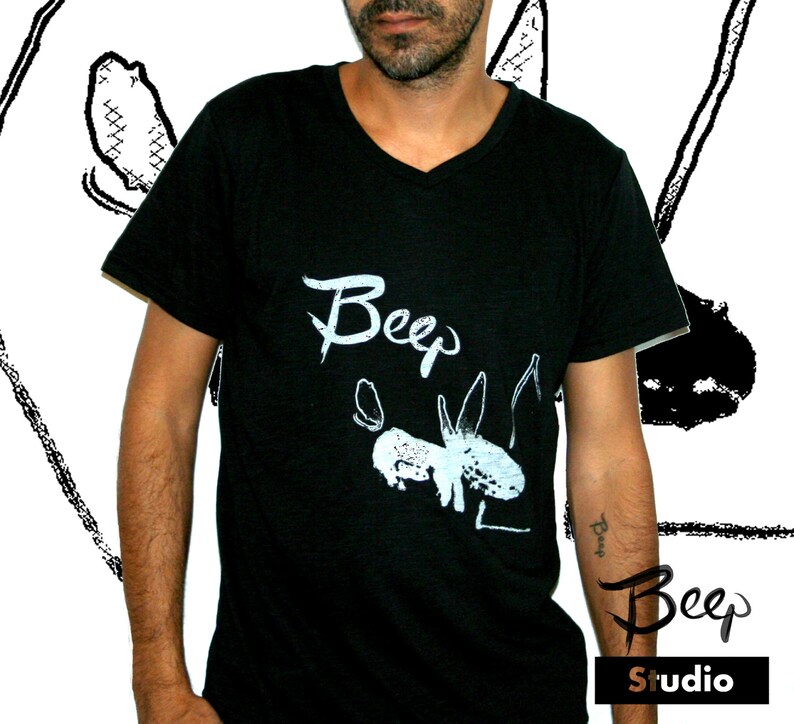 May include: Black V-neck t-shirt with the word "Beep" in white script and a white illustration of a creature. The shirt also features the text "Beep Studio" in a stylized font.