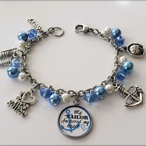 Puede incluir: Un brazalete de plata con cuentas azules y blancas y dijes, incluyendo un ancla, un coraz&oacute;n con las palabras "Amo a mi marinero", una bandera y un dije redondo con las palabras "Mi marinero ancl&oacute; mi coraz&oacute;n".