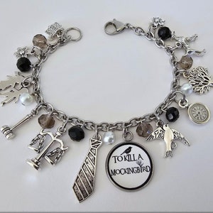 May include: A silver charm bracelet with various charms, including a gavel, scales of justice, a tie, a bird, a tree, a clock, and a round charm with the text "To Kill a Mockingbird".