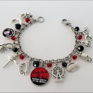 May include: A silver charm bracelet with red and black beads. The charms include a crescent moon, sunglasses, a knife, a set of teeth, a Ferris wheel, a boombox, a car, and a round charm with the text "Santa Carla Murder Capital of the World".