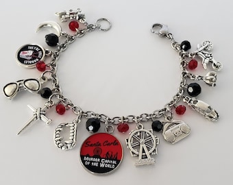 May include: A silver charm bracelet with red and black beads. The charms include a crescent moon, sunglasses, a knife, a set of teeth, a Ferris wheel, a boombox, a car, and a round charm with the text "Santa Carla Murder Capital of the World".