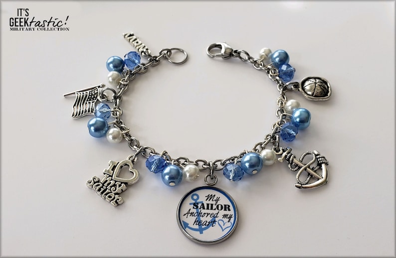 Puede incluir: Un brazalete de plata con cuentas azules y blancas y dijes, incluyendo un ancla, un coraz&oacute;n con las palabras "Amo a mi marinero", una bandera y un dije redondo con las palabras "Mi marinero ancl&oacute; mi coraz&oacute;n".